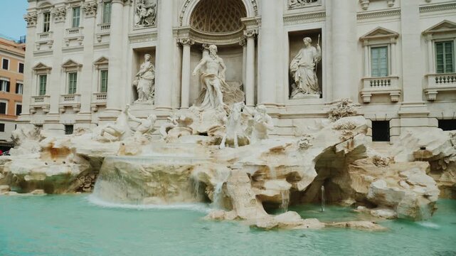 Low angle panoramic view of Trevi Fountain architecture with water cascades and historical marble sculptures in Rome.