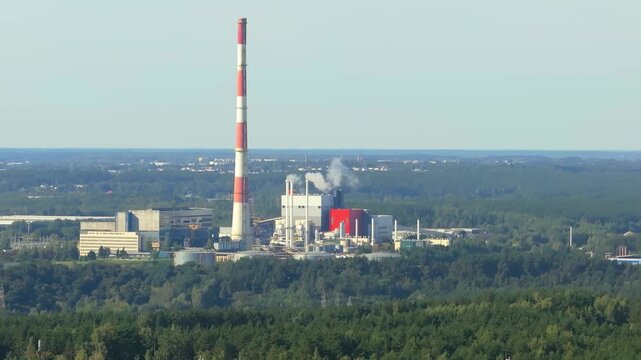 Industrial power plant with tall chimney stack emitting smoke in forest