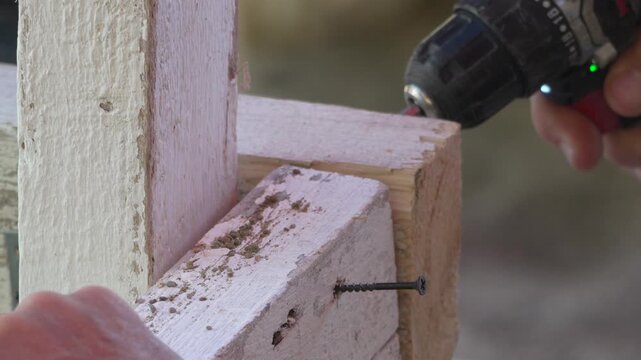 Power drill fastening black metal screw into rustic white timber beam at residential renovation site. Static extreme close-up shot.