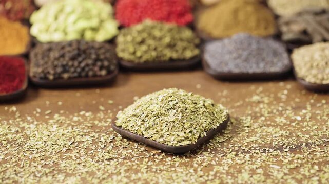 dried oregano leaves flakes origanum vulgare in a small wooden dish on a table filled with colorful spices.