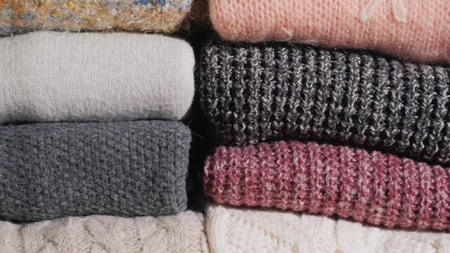 Close up camera panning across stacks of neatly folded warm knit sweaters in various textures and winter colors.