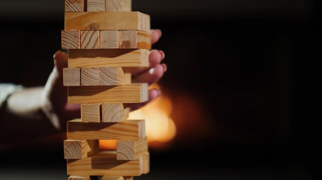 Person carefully removing wooden block from unstable Jenga tower near fireplace footage.