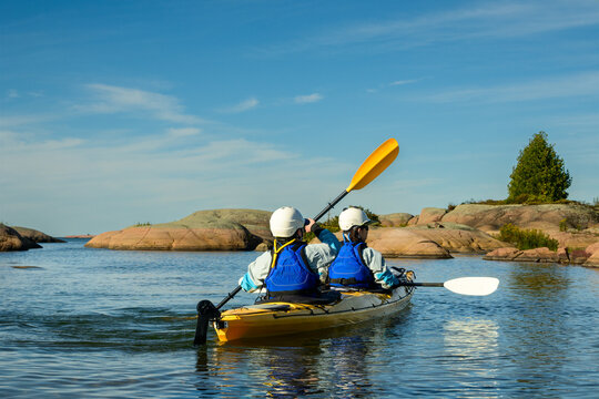 Two helmeted paddlers in a yellow tandem kayak paddle together past pink granite islands in morning light with copy space on Georgian Bay, Ontario, Canada