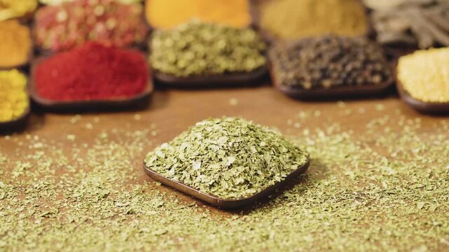cilantro leaves flakes or coriander leaf in a square bowl on a wooden table, surrounded by various spices and herbs.