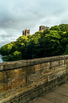 Durham Cathedral towers above the River Wear seen over a sunlit stone bridge parapet