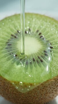 Fresh kiwi fruit cut in half with clear syrup pouring over the vibrant green flesh and seeds
