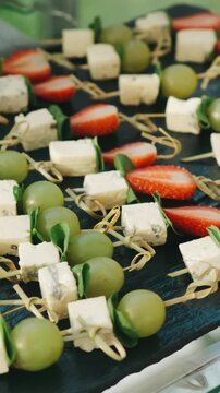 bamboo picks with green grapes, basil leaves, herb cheese cubes, and strawberry halves on dark slate, shifting