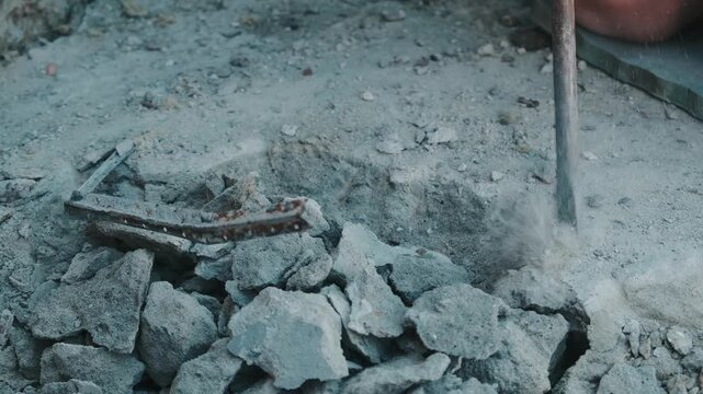 rotary hammer and chisel break cracked concrete slab, releasing dust and exposing rusted rebar in ground view.