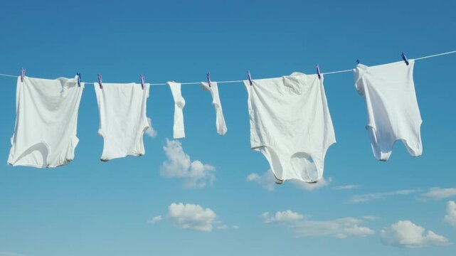 White laundry drying on clothesline against blue sky background with clouds.