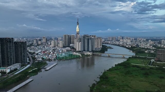 Daytime aerial view of Landmark 81 and dense residential towers beside a broad river in Ho Chi Minh City beneath cloudy skies