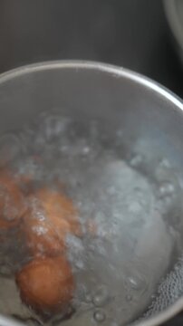Top-down view of brown eggs boiling in stainless steel pot with vigorous bubbles, frothy foam around shells, and rising steam, domestic kitchen scene for cooking and recipe preparation