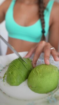 Close-up of hands slicing ripe avocado on plate while person in turquoise sports bra appears in soft background
