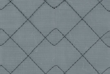 Fototapeta premium Quilted blue fabric with dark thread marking large overlapping stitched diamonds, a woven textile texture with short loose fibers and a repeated mesh beneath the seams