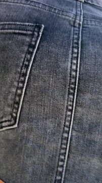 Low-angle close-up of dark denim mini skirt and tanned thighs as hand rests at back pocket on sunlit urban sidewalk