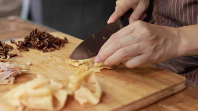 Person slicing bean curd skin on a wooden board