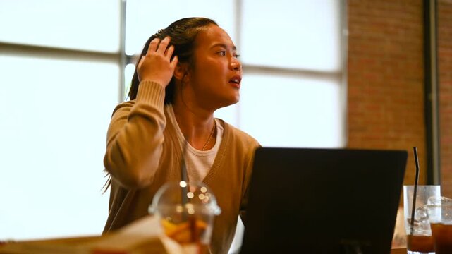 A woman gestures in conversation with another person across a cafe table. The woman faces the other diner as a laptop, cold drinks, glassware, and brick walls surround the wooden table.