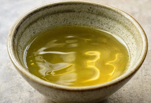 A rustic ceramic bowl filled with golden green tea reflecting light on a textured surface