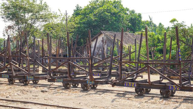 Empty traditional rusty metal sugarcane rail cars parked on narrow tracks at historical Rendeng Sugar Mill in Kudus, Central Java, Indonesia, used for transporting sugar cane during harvest.