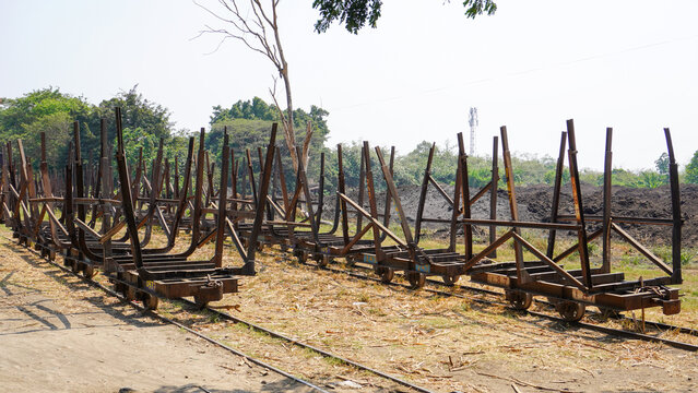 Empty traditional rusty metal sugarcane rail cars parked on narrow tracks at historical Rendeng Sugar Mill in Kudus, Central Java, Indonesia, used for transporting sugar cane during harvest.