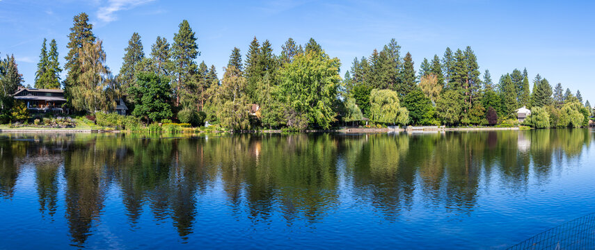 Mirror Pond on the Deschutes River in Bend Oregon reflects evergreen trees and homes along its shoreline.