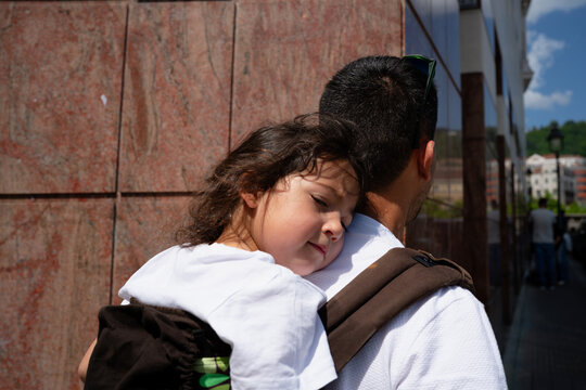 Father carrying sleeping child piggyback on city street