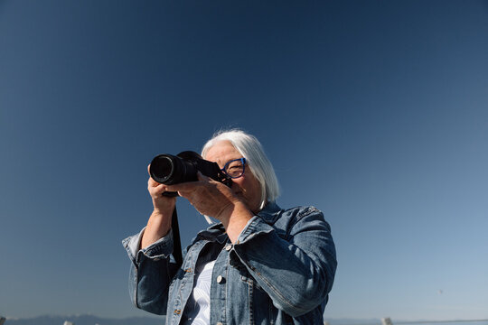 Senior woman photographer shooting with camera outdoors, candid