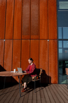 Woman working on laptop at sunlit cafe terrace