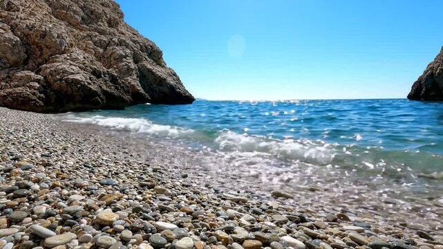 Pebble beach with gentle waves lapping on the shore under a clear blue sky