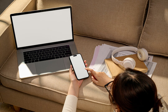 Woman using laptop and smartphone on a sofa, overhead view
