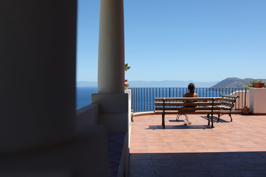 Person sitting on terrace bench facing the sea