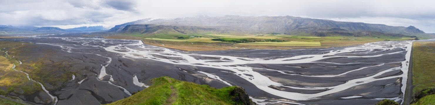Panoramic high angle view of intricate braided glacial river networks flowing through dark volcanic sand plains in Iceland, captured from Stora Dimon mountain.