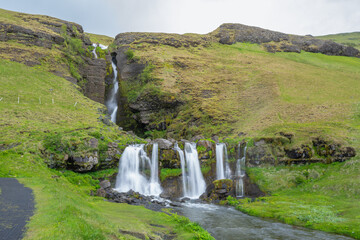Scenic view of Gluggafoss waterfall flowing down a lush green hillside in Iceland, featuring tiered cascades and a running stream. © twabian