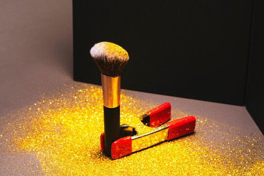 A makeup brush, covered in gold glitter  in front of a photo backdrop