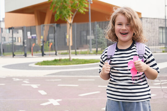 Child stands smiling outside school with backpack