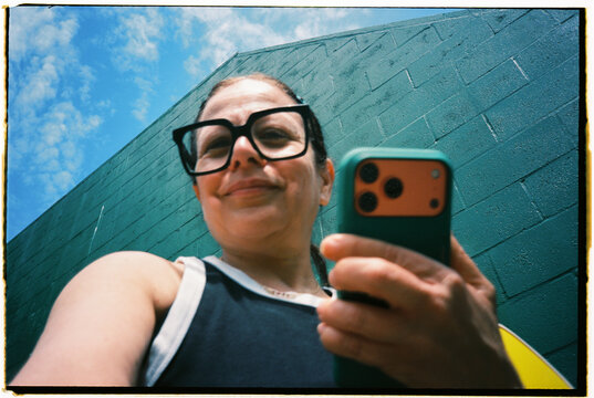 Woman Takes a Selfie in Front of a Green Wall on a Sunny Day