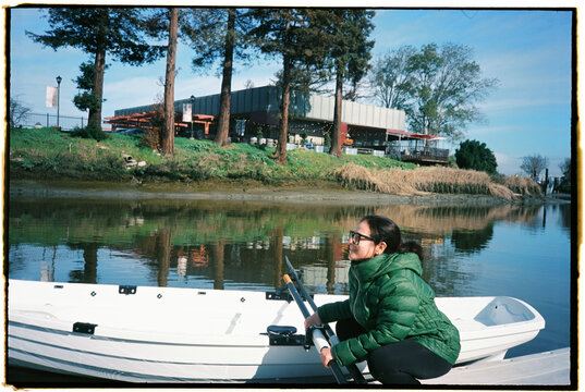 Woman Sitting in a Boat by a River Near a Building in Daylight