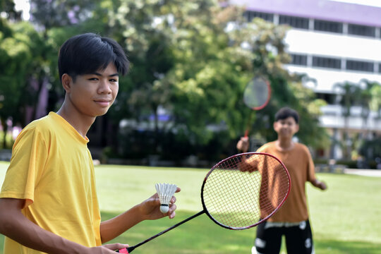 A young man in a yellow shirt holds a badminton racket and shuttlecock on a grassy field.