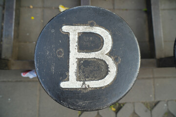 Close-up of a painted white letter B on a round black metal street bollard cap. © Alvi Prasetya