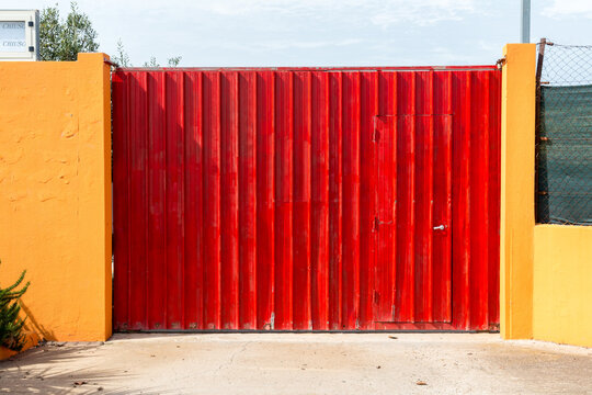 Italy, Sardinia, Oristano.  Bright red, corrugated steel gate across the entrance to an industrial facility.