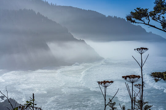 Beautiful scenic view of a stormy ocean and misty mountains with sun rays through fog