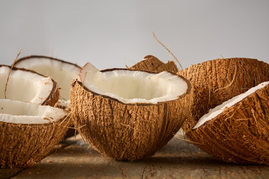 broken coconut halves on rustic wooden table, brown hairy shell and white fresh meat tropical fruit in close-up side view with copy space, healthy vegan food ingredient