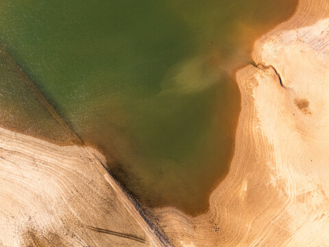An aerial view of a drying reservoir with receded water levels exposing arid, cracked soil due to extreme drought and climate change