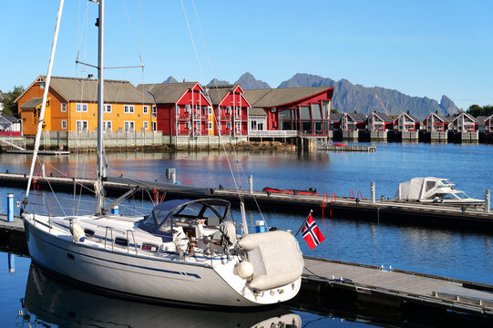 Sailboat at a pier in Svolvaer harbor in the Lofoten Islands with calm water, colorful houses and distinctive mountains beneath a clear blue sky.