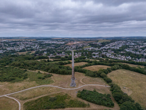Aerial view of the Bodmin Beacon monument surrounded by green fields, walking paths, and the town of Bodmin in the background under a cloudy sky in Bodmin, Cornwall, United Kingdom.