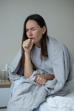 Sick woman resting in bed with symptoms of fever, runny nose and cough during an illness