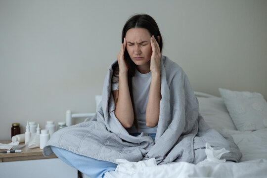 Sick woman resting in bed with symptoms of fever, runny nose and cough during an illness