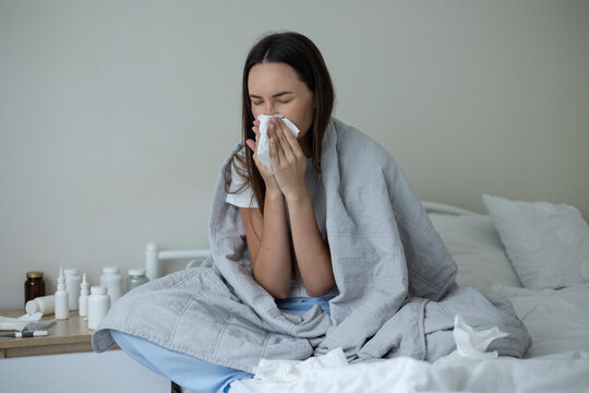 Sick woman resting in bed with symptoms of fever, runny nose and cough during an illness