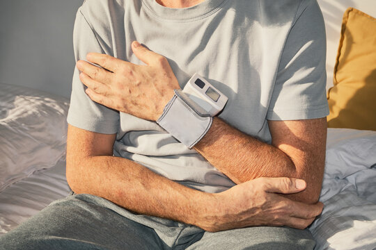 Senior man checking blood pressure on his wrist while sitting on bed at home