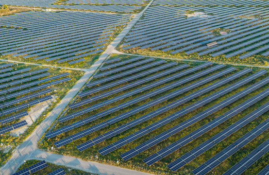 Aerial view of a massive photovoltaic solar power plant with long parallel rows of solar panels and service roads in Trino, Piedmont, Italy.