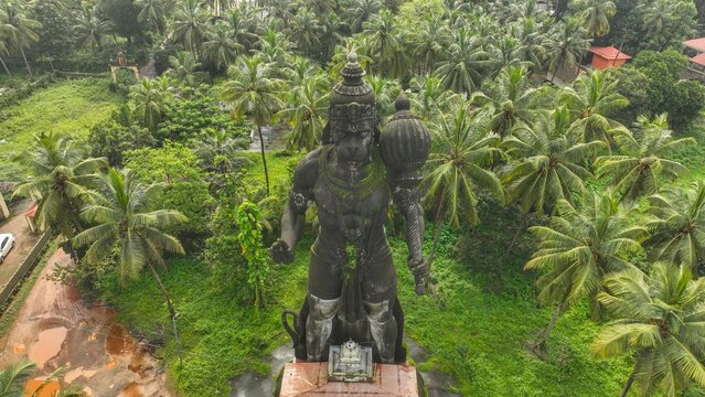 Aerial view of the large stone statue of Lord Hanuman holding a mace, surrounded by lush palm trees and dense greenery in Udupi, Karnataka, India.